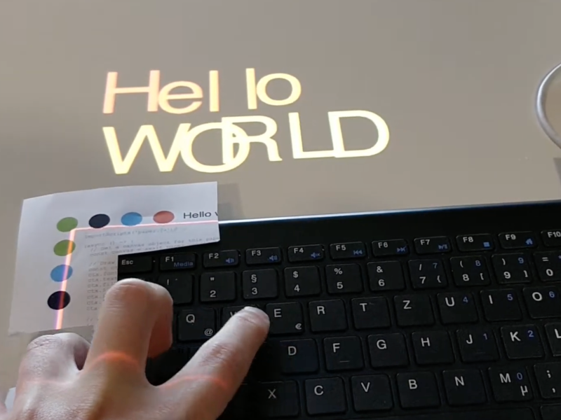 a keyboard on a table that has the phrase 'Hello WORLD' projected above it